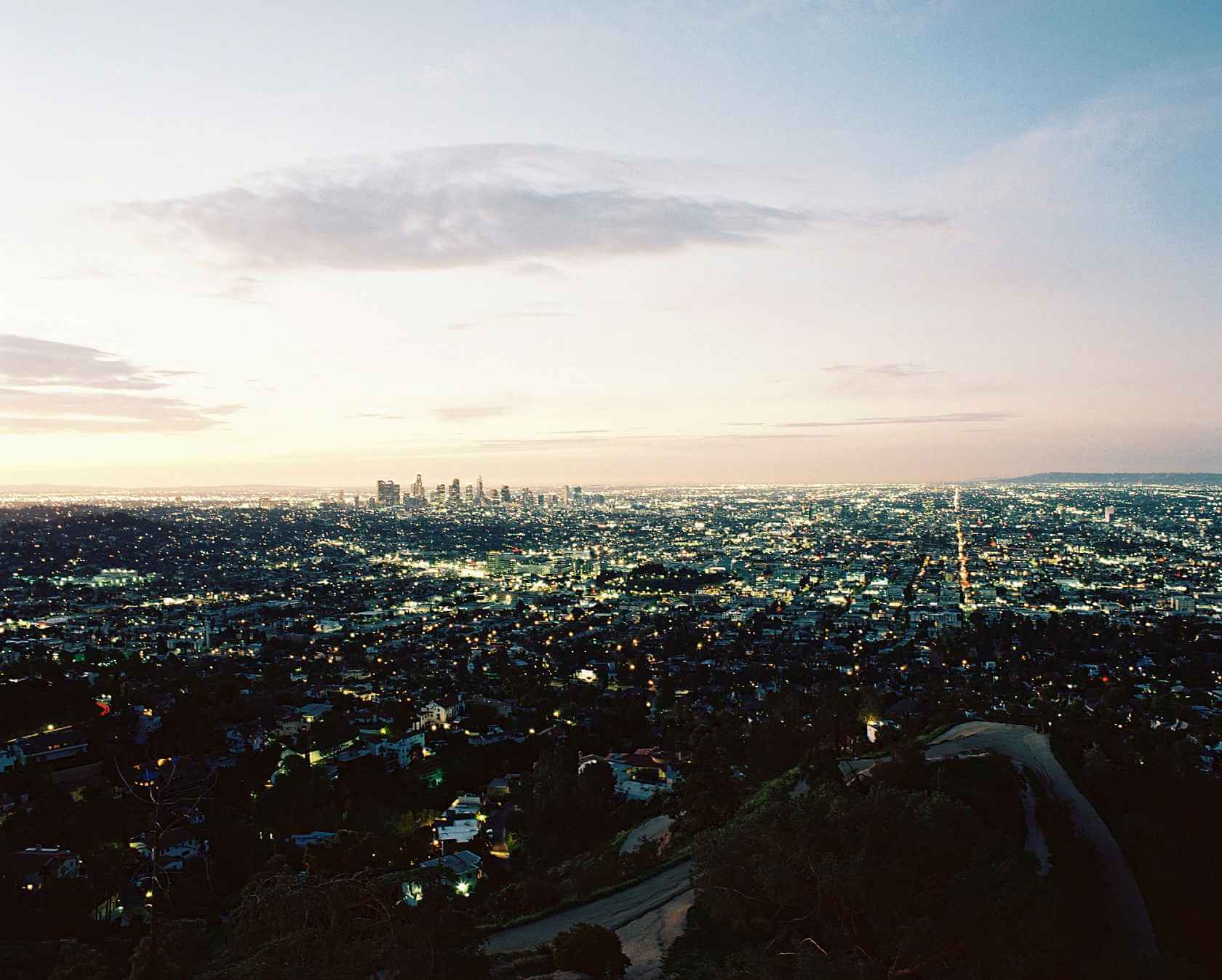 A stunning aerial view of a vibrant city skyline at dusk, showcasing twinkling lights and a soft evening sky.