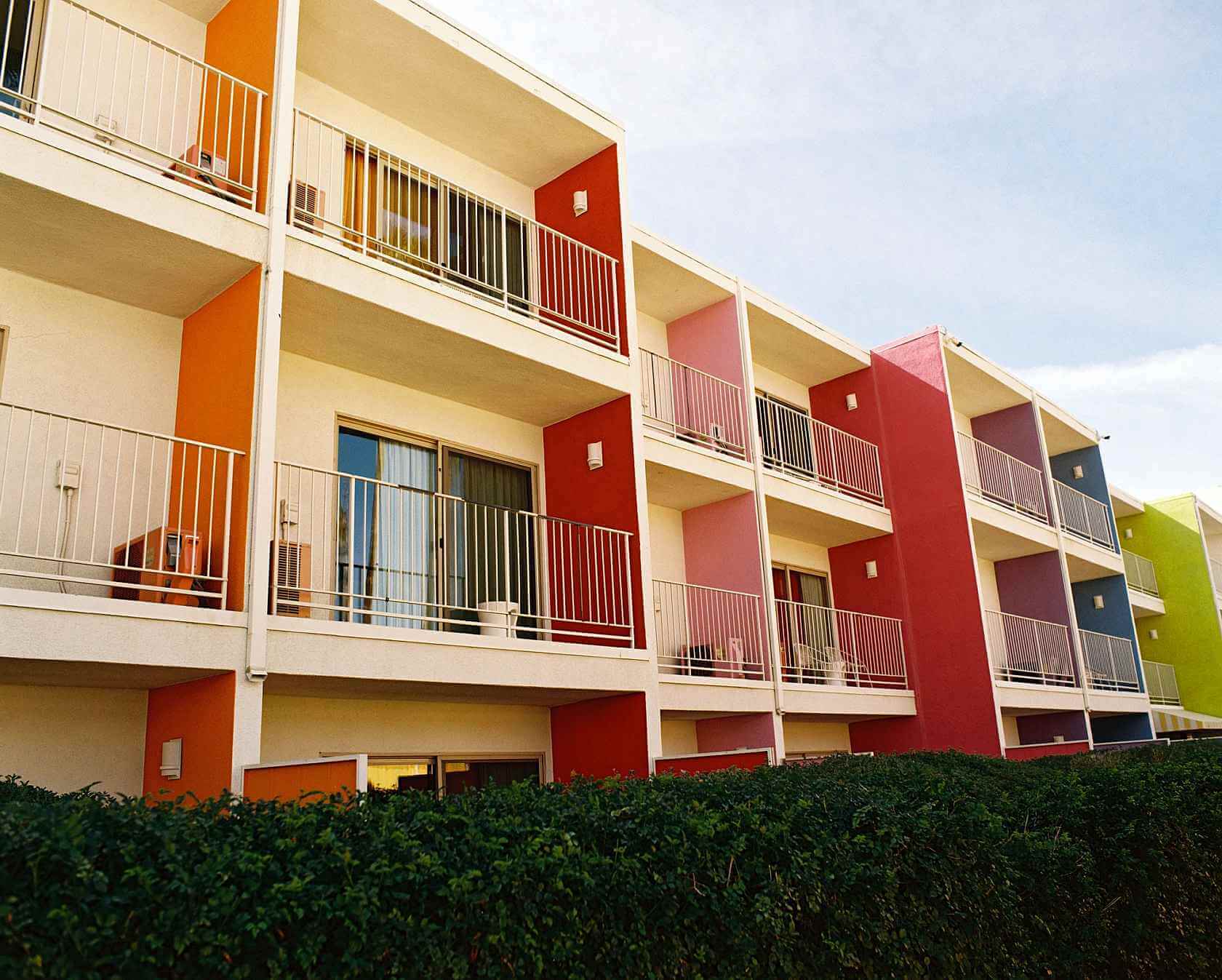 Colorful apartment building with multiple balconies and green hedges in the foreground.