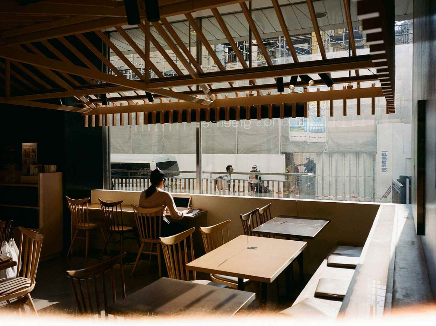 Interior of a cafe with a woman sitting at a table, bright natural light streaming through large windows.