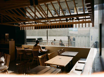 Interior of a cafe with a woman sitting at a table, bright natural light streaming through large windows.