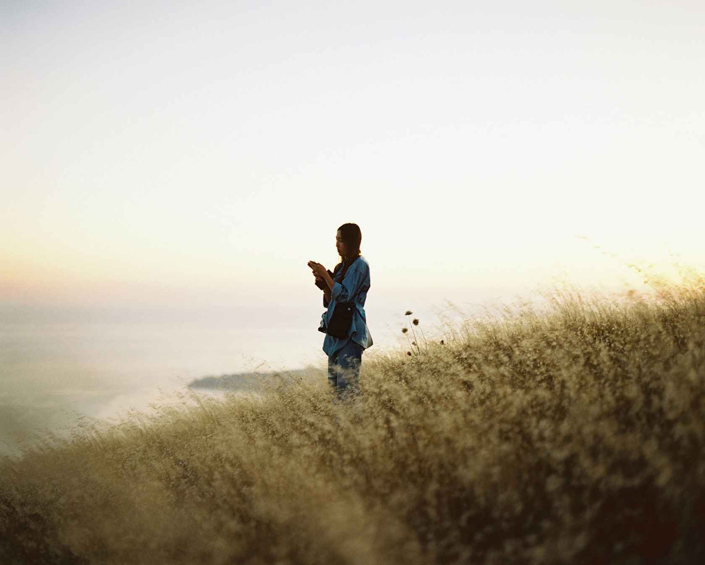 Person silhouetted against a sunset holding a camera on a grassy hill