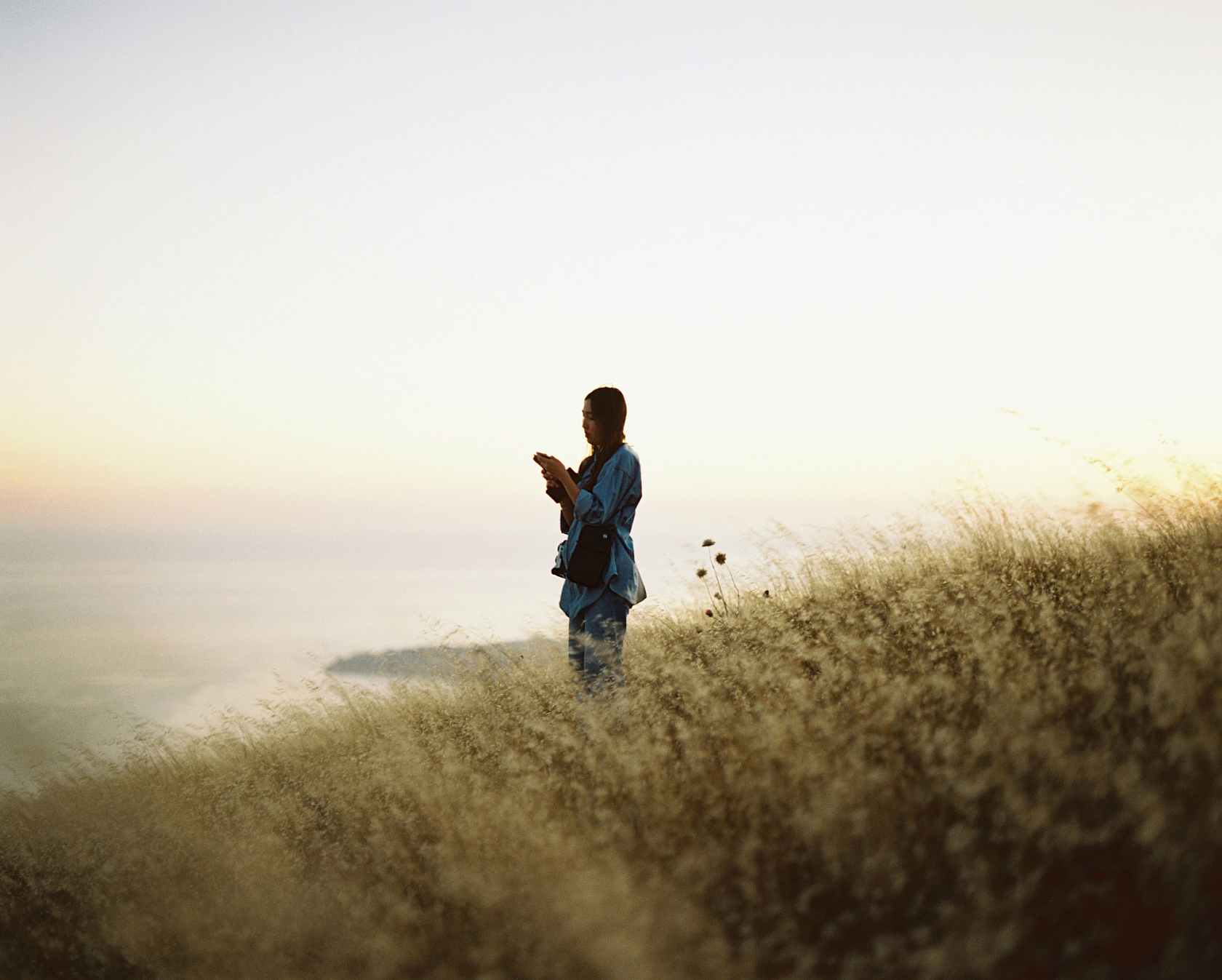 Person silhouetted against a sunset holding a camera on a grassy hill