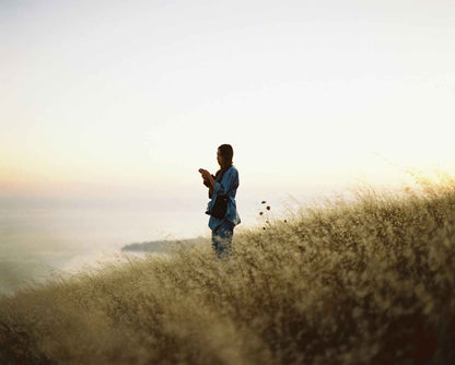 Person silhouetted against a sunset holding a camera on a grassy hill
