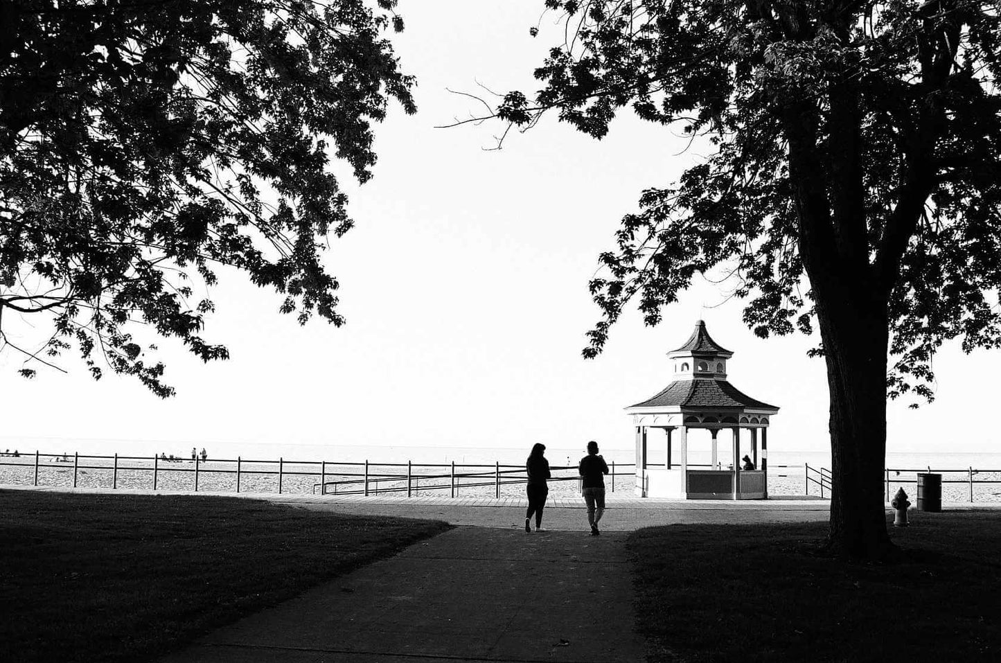 Two people walking towards a gazebo at the beach, captured in striking black and white.