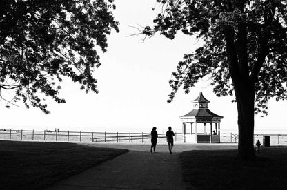 Two people walking towards a gazebo at the beach, captured in striking black and white.