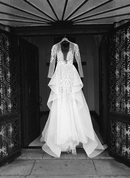 Elegant white wedding dress with lace details hanging at an ornate doorway, showcasing bridal fashion.