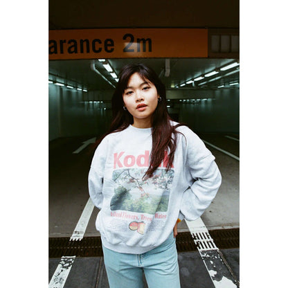 A woman wearing a Kodak sweatshirt stands in a parking garage with a 2m clearance sign.
