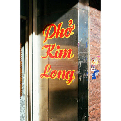 Pho Kim Long restaurant sign in vibrant yellow lettering on a reflective surface.
