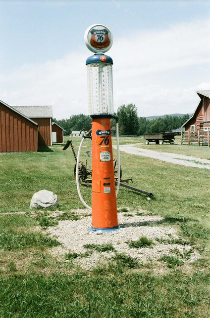 Vintage orange and blue 76 gas station pump in a rural setting with barns in the background.