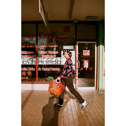 A person in a floral shirt and orange bag walking in front of a Chinese restaurant with delivery signage.